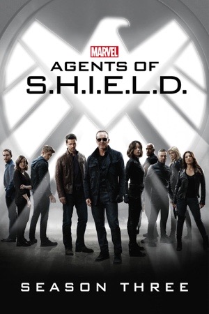 The cast in grey and white in front of a huge metallic S.H.I.E.L.D. shield.